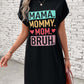 Woman wearing a black short sleeve mini tee dress with colorful text "MAMA. MOMMY. MOM. BRUH." against a brick wall background.