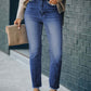 Woman wearing high waist raw hem skinny jeans and beige sweater, holding a clutch, outdoors.