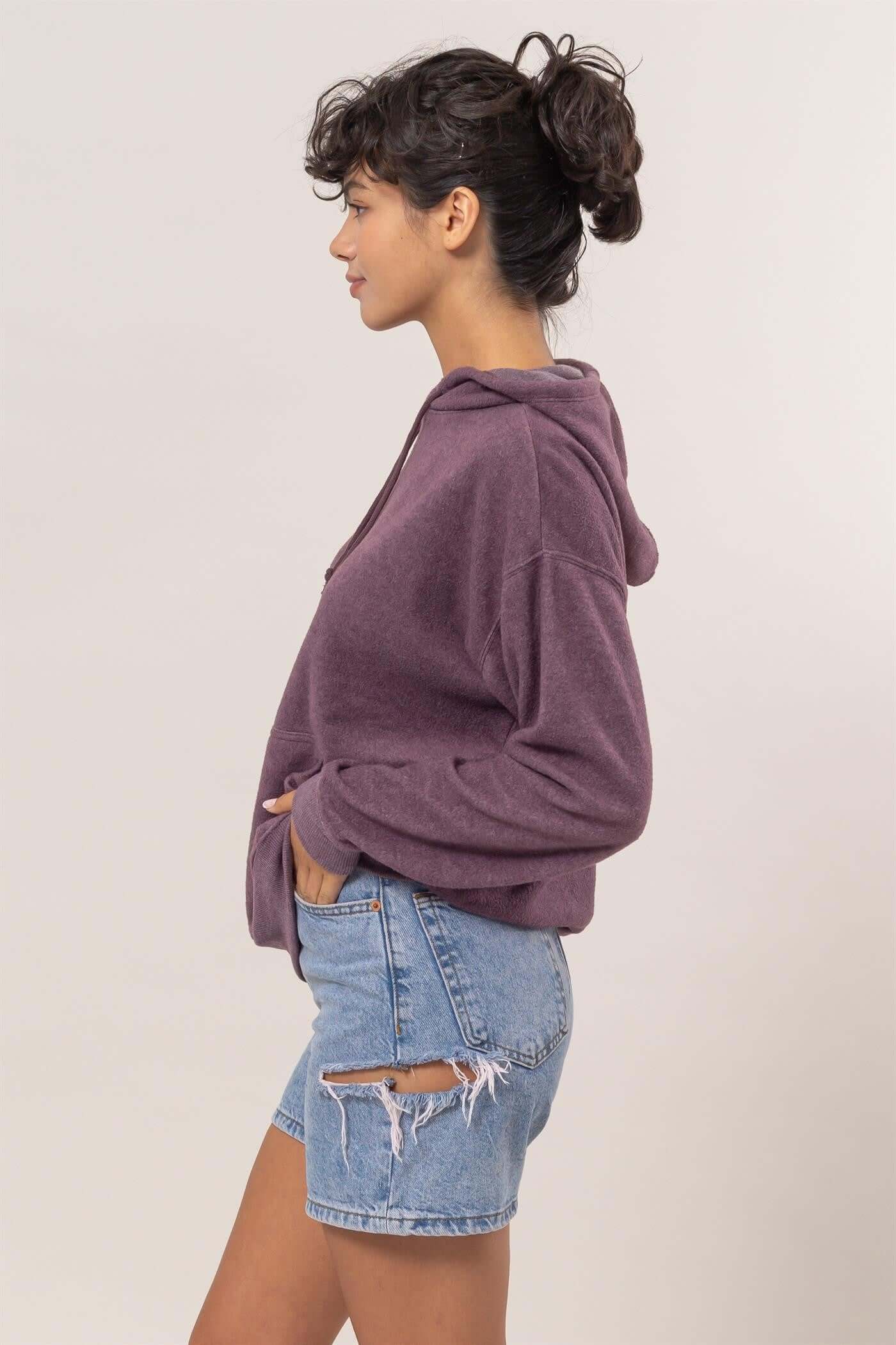 Woman wearing a cozy purple brushed hoodie with kangaroo pocket and denim shorts, showcasing casual style.