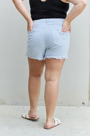 Woman wearing Katie High Waisted Distressed Shorts in Ice Blue by Risen Jeans, showcasing the trendy and comfortable back view.