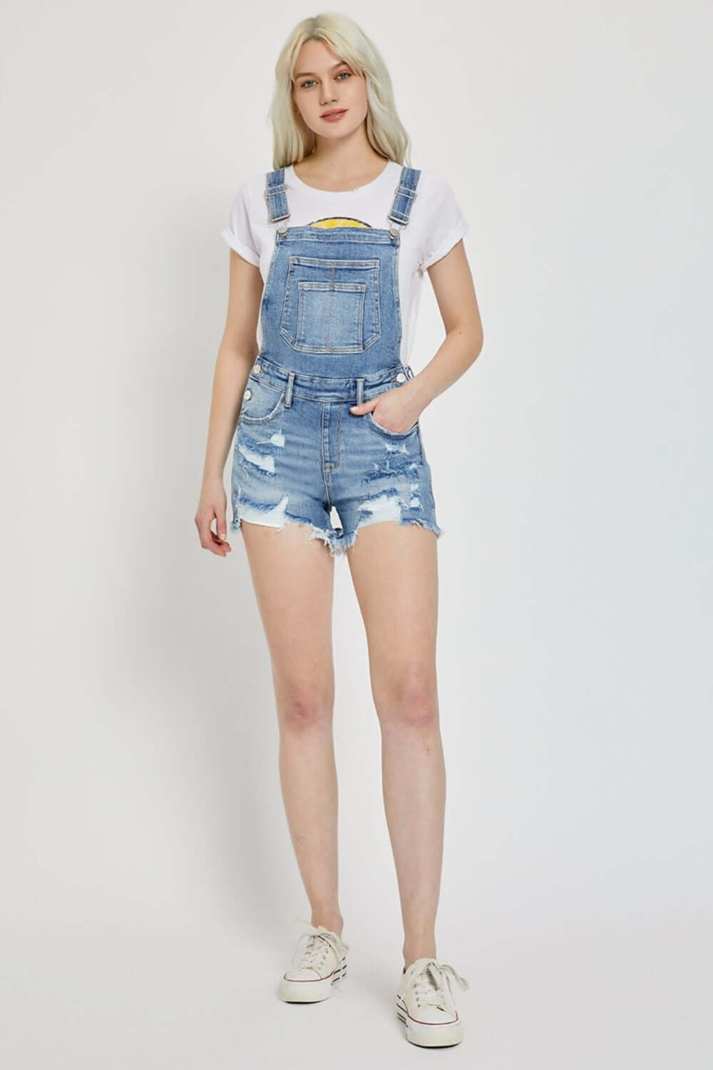 Person wearing Risen Jeans distressed raw hem denim overalls, showcasing trendy and edgy casual style.