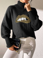 Woman wearing Bella Road Lip Turtleneck Sweater in black with bold lip design, paired with white pants, holding a black clutch.