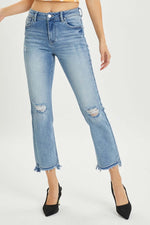 Risen high rise distressed cropped straight jeans with frayed hems, paired with black heels, showcasing trendy and edgy style.