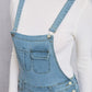 Close-up of distressed washed denim overalls with pockets, worn over a white ribbed turtleneck sweater.