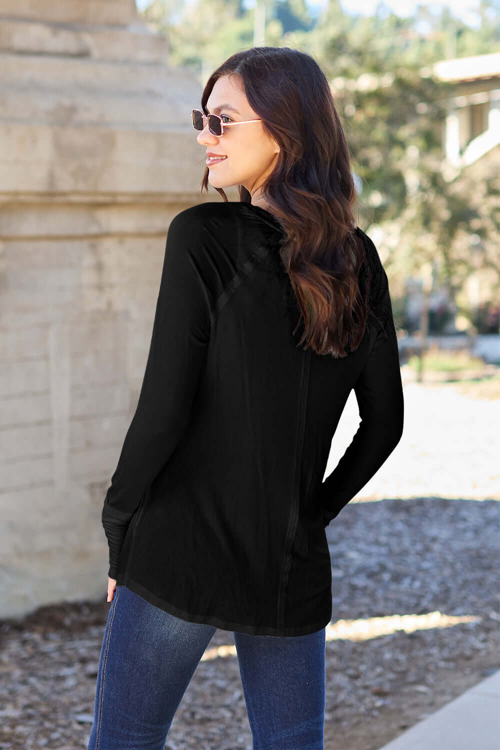 Woman wearing a black round neck long sleeve t-shirt and jeans standing outdoors, showcasing the back view of the t-shirt