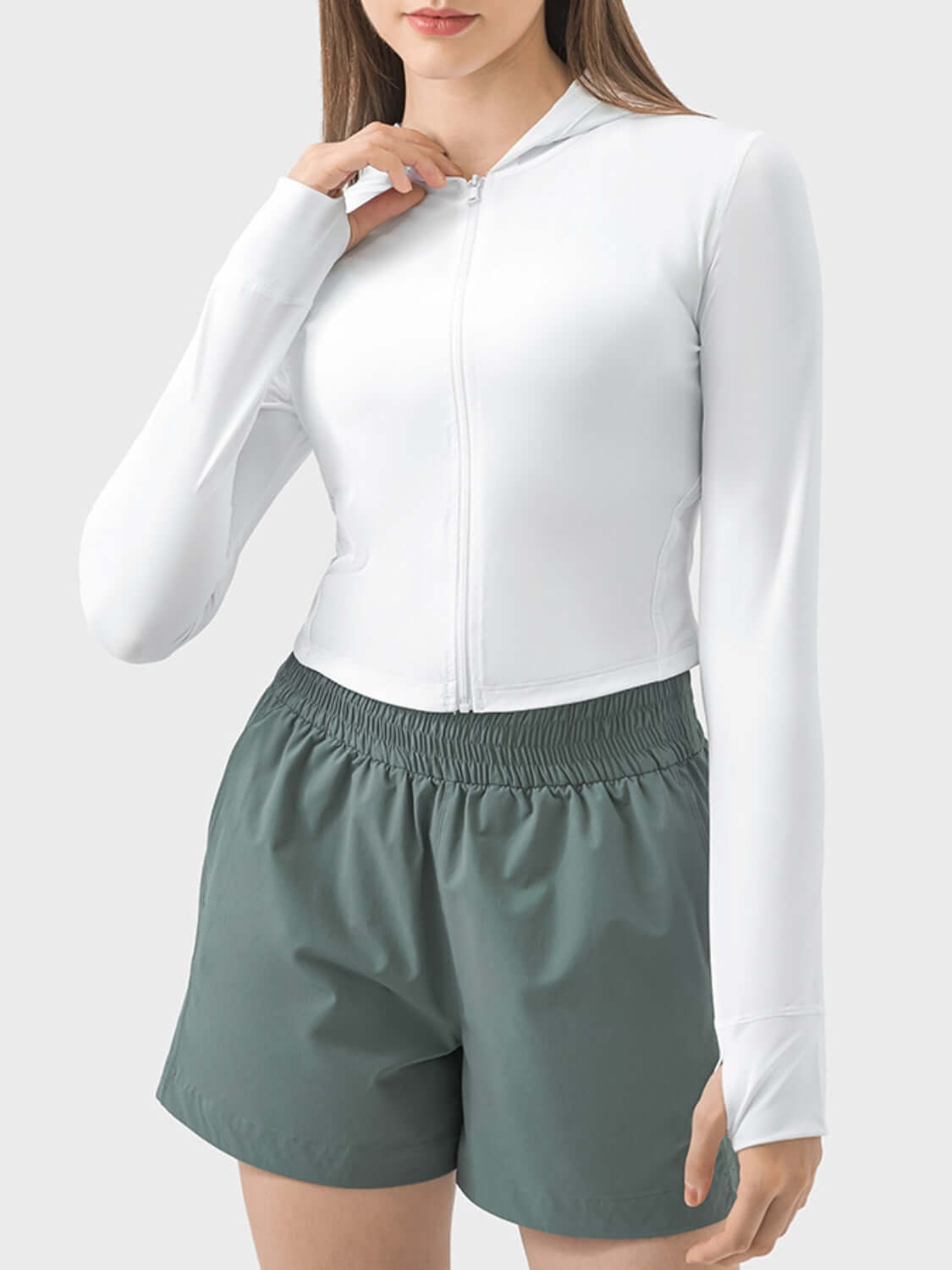 Model wearing white Millennia Zip Up Hooded Long Sleeve Active Outerwear with green shorts, showcasing stylish active fashion.