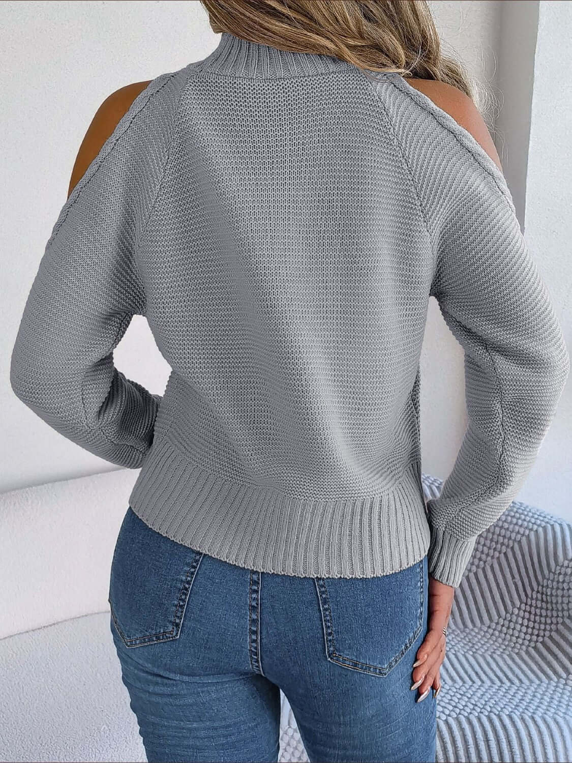 Woman wearing Bella Road Cable-Knit Turtleneck Cold Shoulder Sweater in gray, paired with jeans, showing back view. Cozy and stylish.