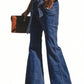 Woman wearing blue tied flare jeans with pockets and holding a brown clutch.