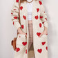 Woman wearing Bella Road Heart Open Front Long Sleeve Cardigan with red heart patterns and pockets, paired with white top and beige pants