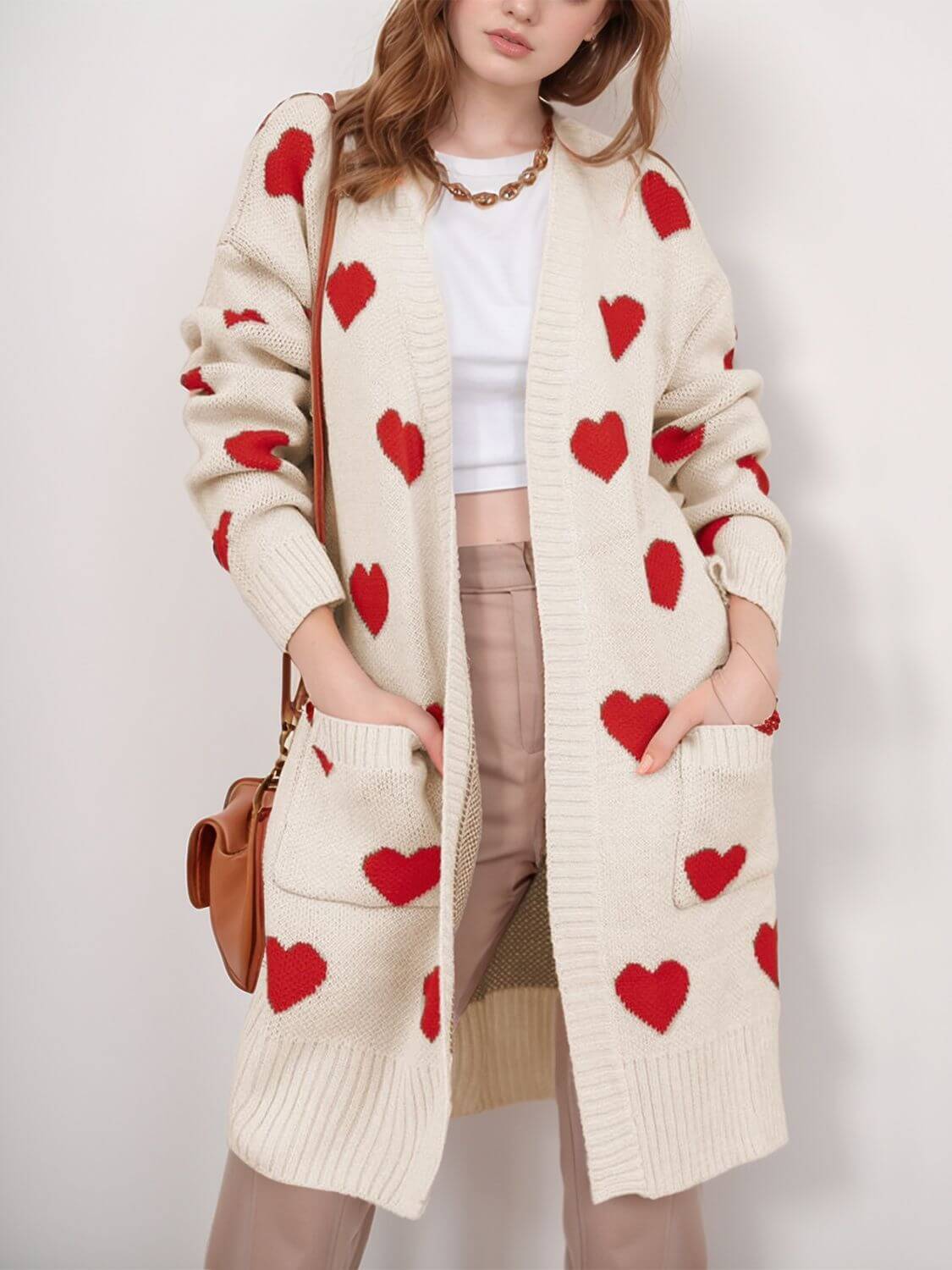 Woman wearing Bella Road Heart Open Front Long Sleeve Cardigan with red heart patterns and pockets, paired with white top and beige pants