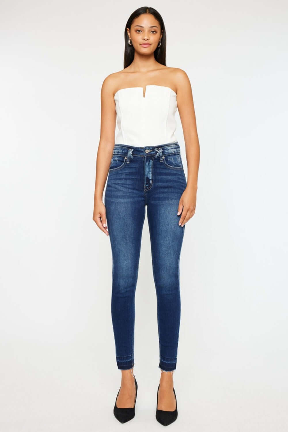 Woman wearing Kancan high-rise ankle skinny jeans with a double waistband and release hem, paired with a white strapless top.