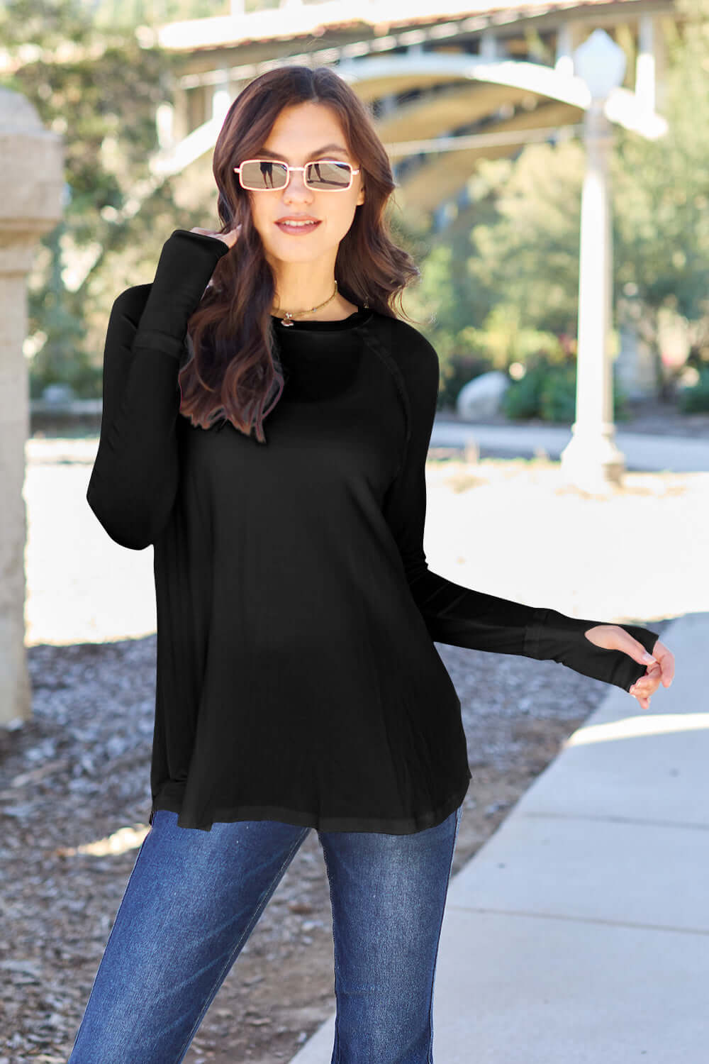 Woman wearing a black round neck long sleeve T-shirt paired with blue jeans and sunglasses outdoors