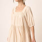 Woman wearing a stylish pintuck detail tie back mini dress in soft beige, ideal for casual or special occasions.