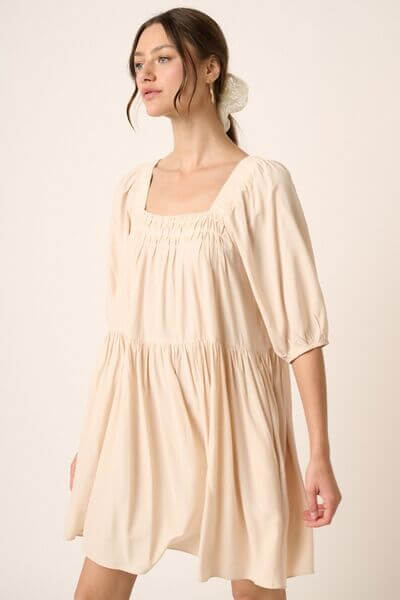 Woman wearing a stylish pintuck detail tie back mini dress in soft beige, ideal for casual or special occasions.