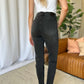 Woman wearing RFM Full Size High Rise Tummy Control Skinny Jeans in black, standing in a modern room.