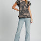 Stylish woman in ruffled landscape print short sleeve French terry top paired with light jeans and heels.