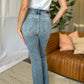 Woman wearing Judy Blue medium rise bootcut jeans in a living room setting, showcasing stylish and comfortable denim fit.