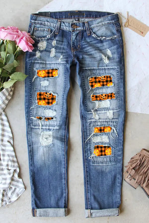 Distressed pumpkin pattern jeans with pockets, slightly stretchy, featuring ripped patches revealing orange and black pumpkin design.