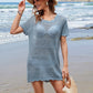 Stylish woman in openwork blue cover-up at the beach, wearing a hat and holding a straw bag, perfect for summer attire.