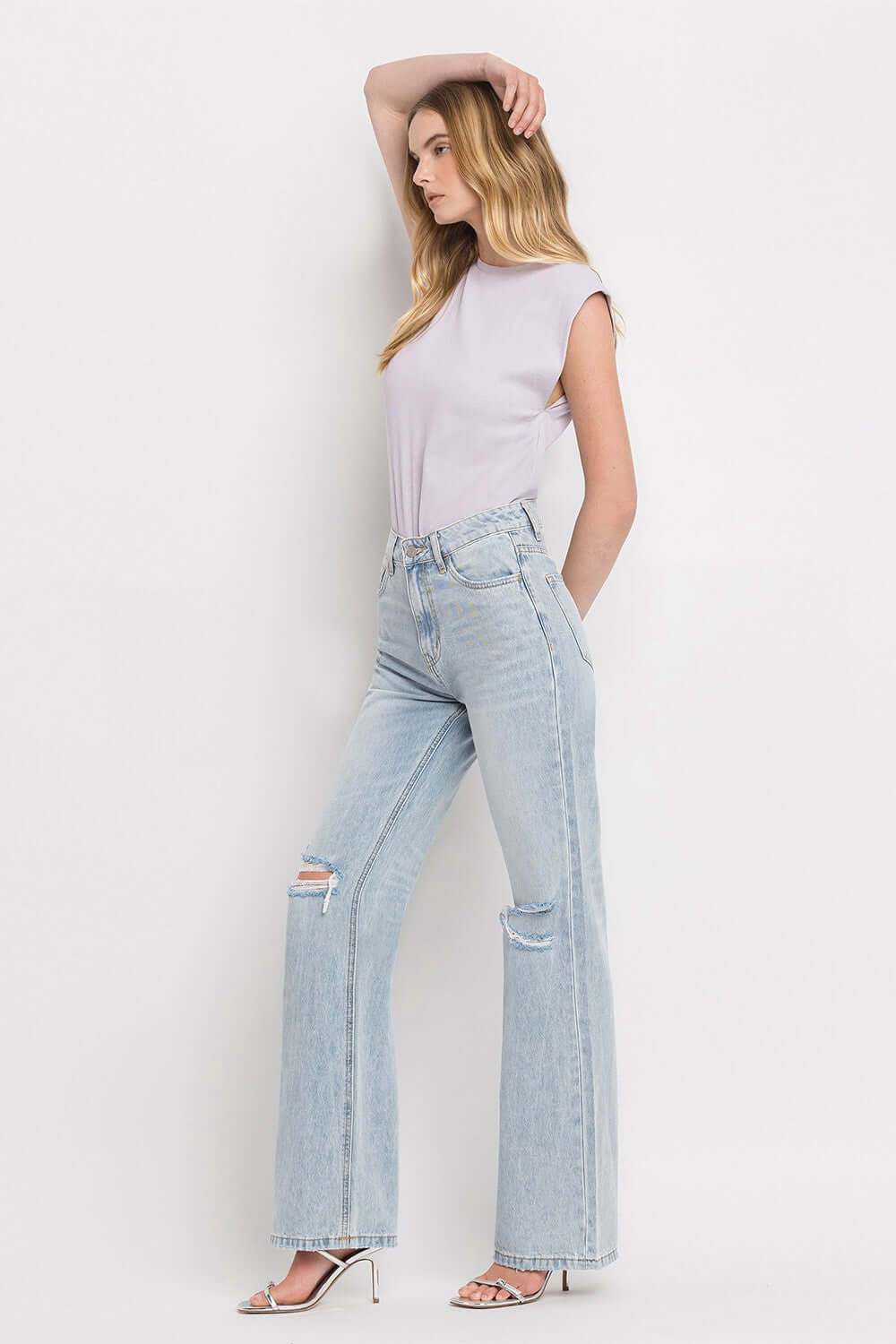 Model wearing 90's Vintage Super High Rise Flare Jeans with distressed knees and a white top, showcasing retro-inspired denim fashion from the 1990s.