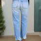 Back view of distressed straight jeans with pockets in light blue, worn by a model standing in front of a green door.