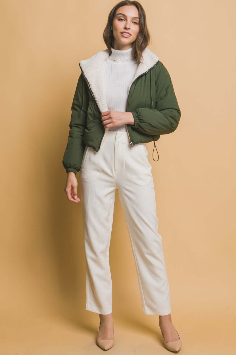 Stylish woman wearing Love Tree cropped hooded Sherpa reversible jacket in green, paired with white pants for a chic casual look.