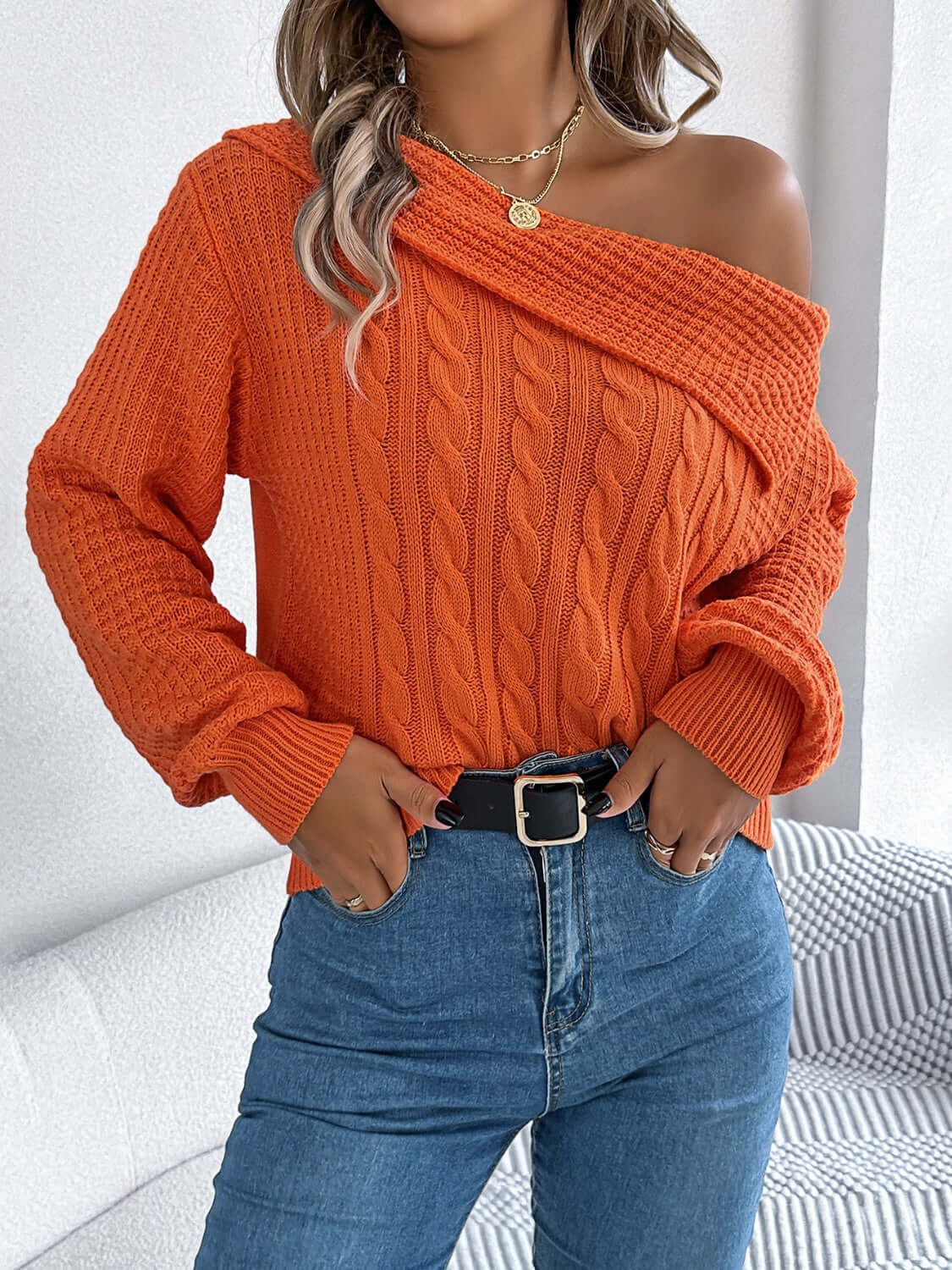 Woman wearing Bella Road Cable-Knit One Shoulder Long Sleeve Sweater in orange, paired with blue jeans.