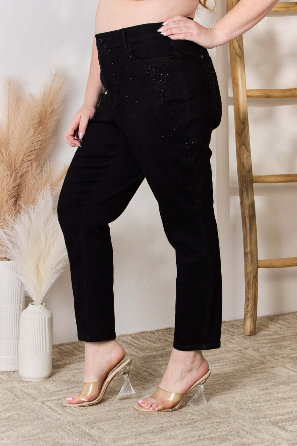 High-waist rhinestone embellished slim black jeans by Judy Blue, shown from the side with hand in pocket