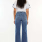 Woman wearing Kancan high-rise slim wide leg jeans in medium wash with trendy hem details, showcasing back view and 5-pocket design.