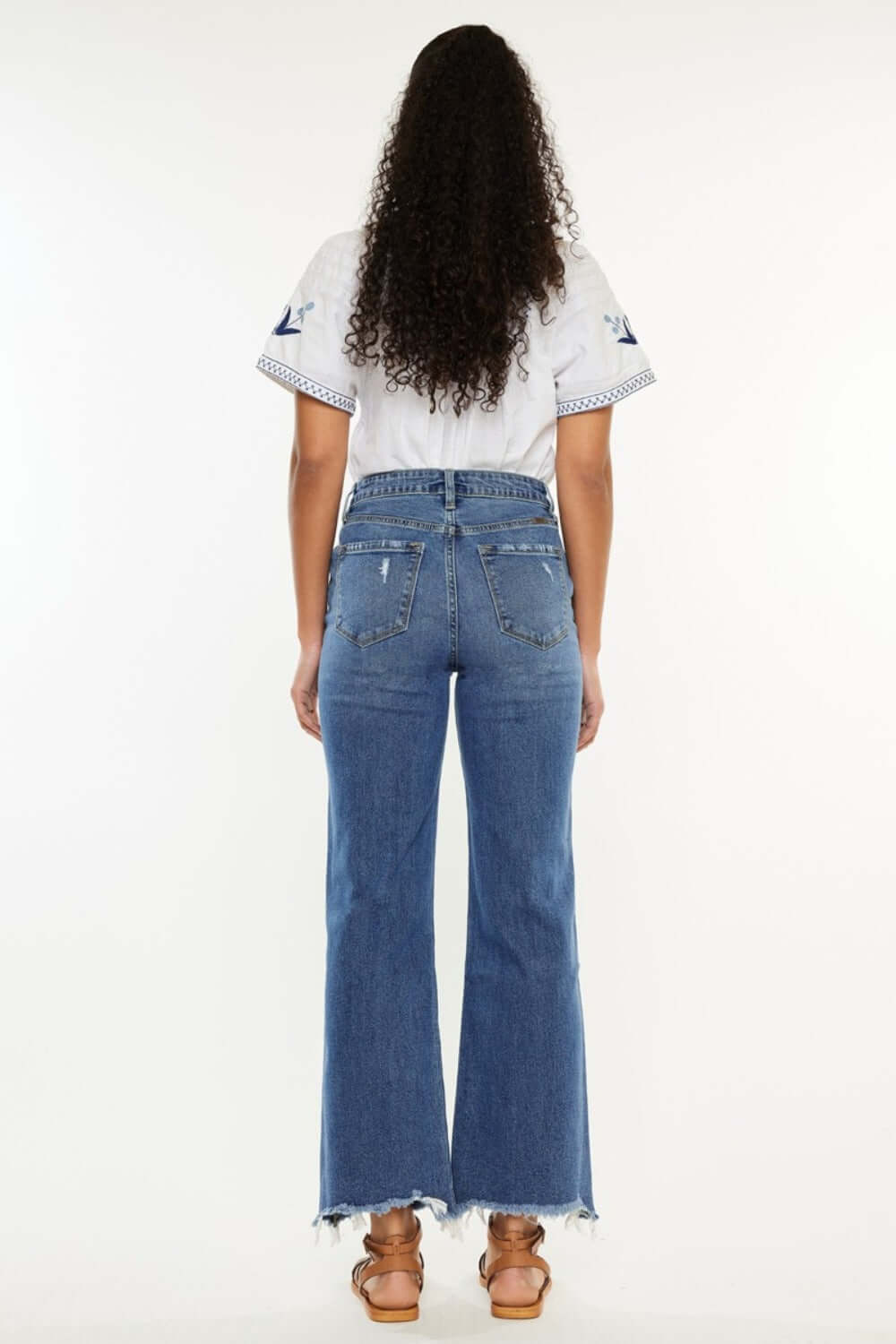 Woman wearing Kancan high-rise slim wide leg jeans in medium wash with trendy hem details, showcasing back view and 5-pocket design.