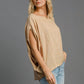 Stylish woman in a tan batwing sleeve knit top, showcasing exposed seams, paired with light blue jeans.