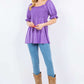 Woman wearing purple ruffled short sleeve smocked blouse with blue jeans and brown boots