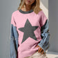 Woman in pink star pattern sweater with denim sleeves, standing outdoors.