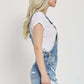 Woman wearing RISEN distressed raw hem denim overalls, side view.