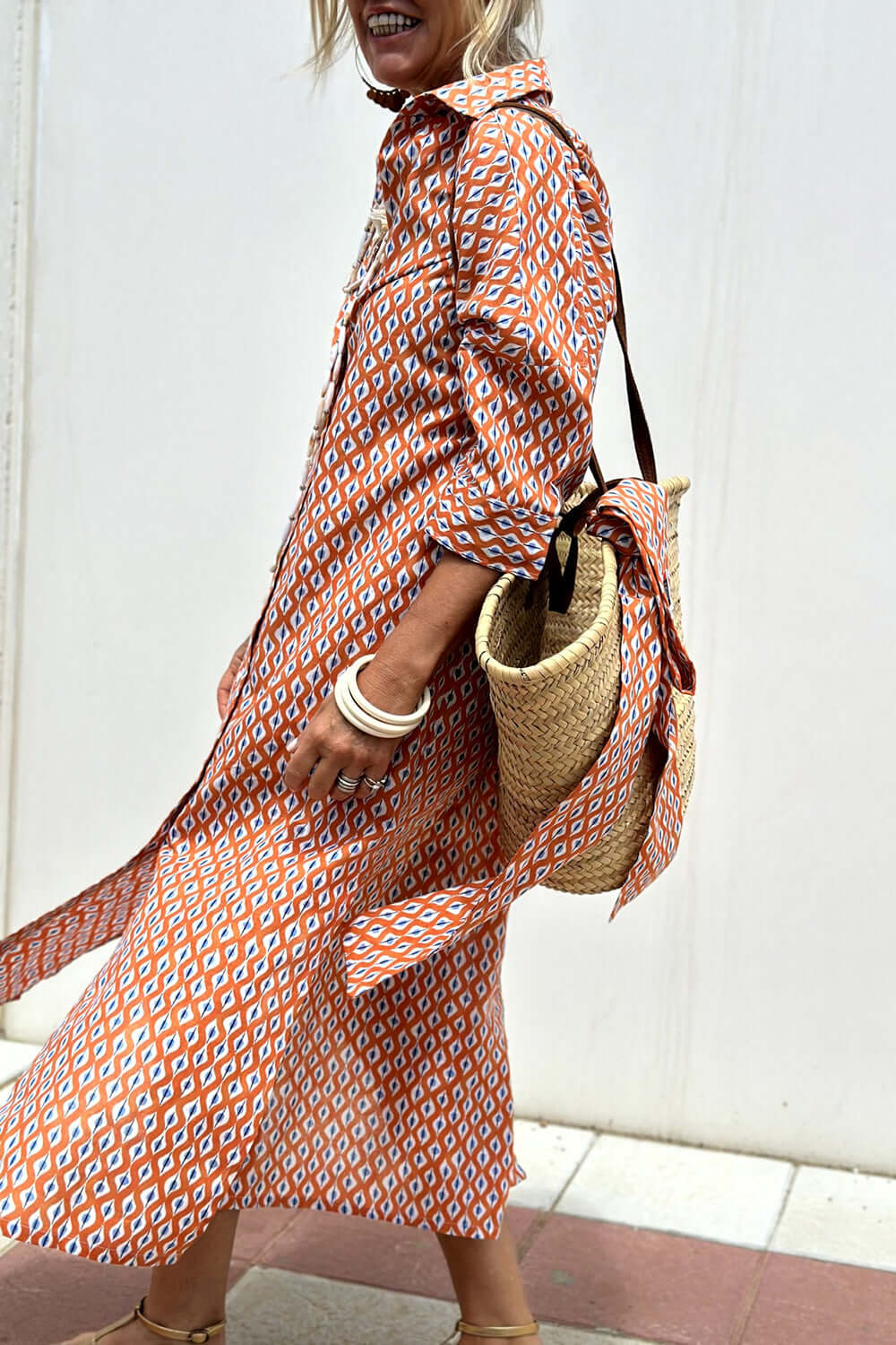 Woman wearing Bella Road Tied Button Up Three-Quarter Sleeve Dress with patterned design, carrying a straw bag