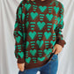 Woman wearing Bella Heart Sweater with turquoise heart design over a brown background and dropped shoulders.