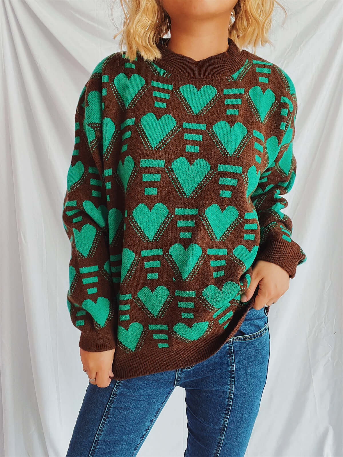 Woman wearing Bella Heart Sweater with turquoise heart design over a brown background and dropped shoulders.