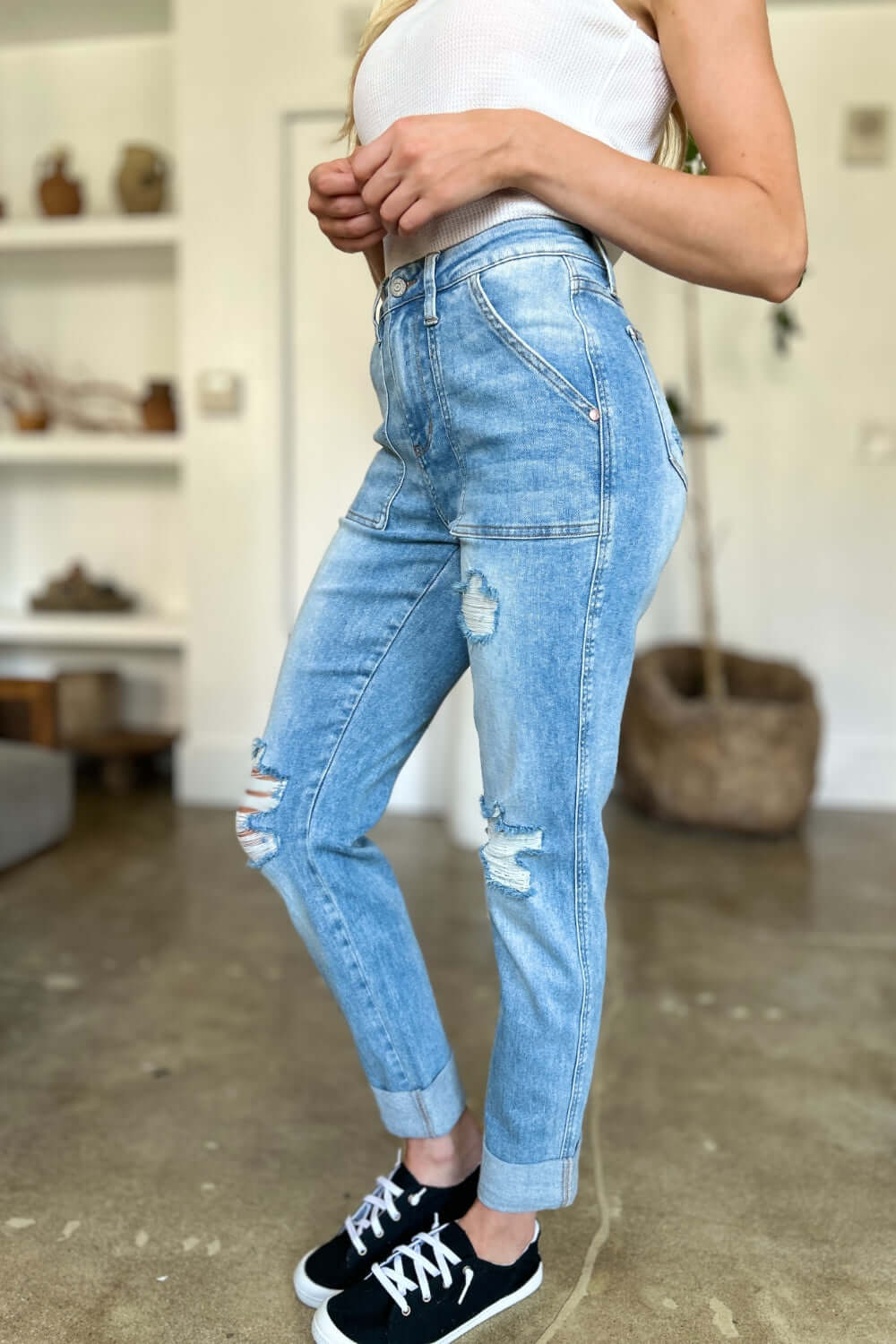 Woman wearing distressed straight Judy Blue jeans with patch pockets, paired with a white top and black sneakers in a casual setting