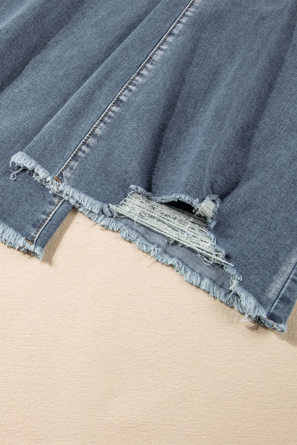 Close-up of distressed raw hem on bootcut jeans, showcasing slightly stretchy denim fabric with a stylish frayed edge.