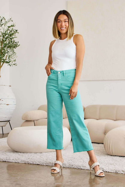 Woman wearing RFM Jeans Crop Chloe Full Size Tummy Control High Waist Raw Hem Jeans in turquoise, paired with a white tank top and sandals.