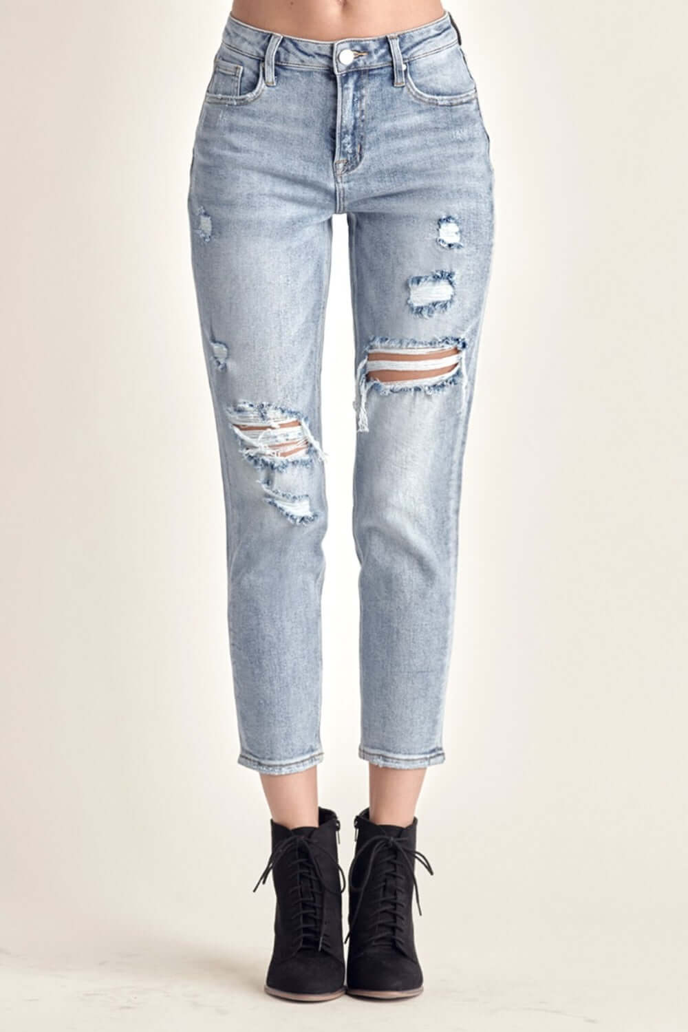 Woman wearing distressed slim cropped jeans with ripped detailing and black ankle boots.