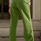 Woman wearing green wide leg jeans with pockets, basic style, 65% cotton, and 35% polyester, standing on steps.