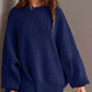 Double Take Side Slit Round Neck Long Sleeve Sweater in navy blue worn by model. Cozy fit, playful side slit design, made with cotton-polyester blend.