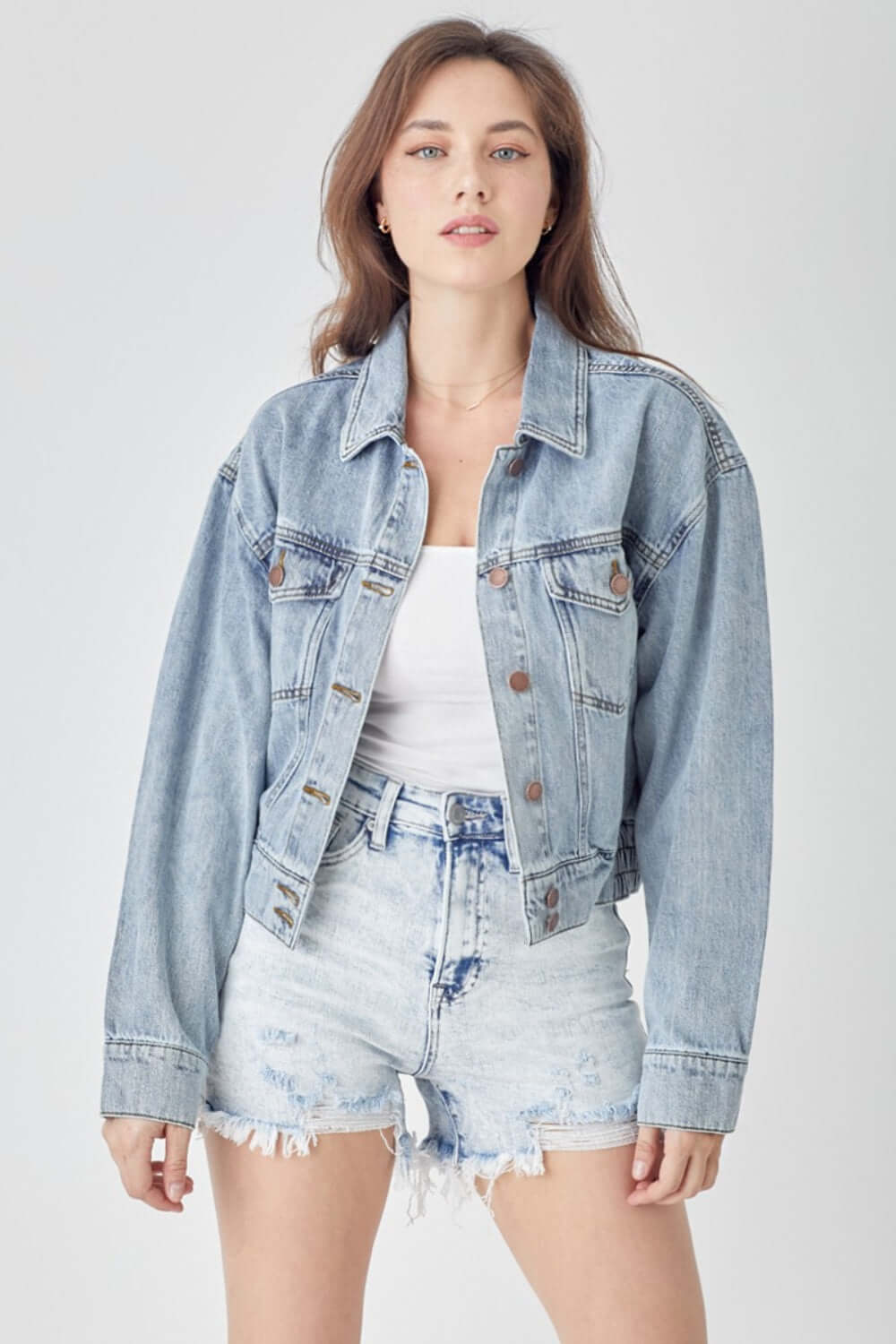 Woman wearing RISEN full size button down cropped denim jacket with white top and distressed denim shorts.