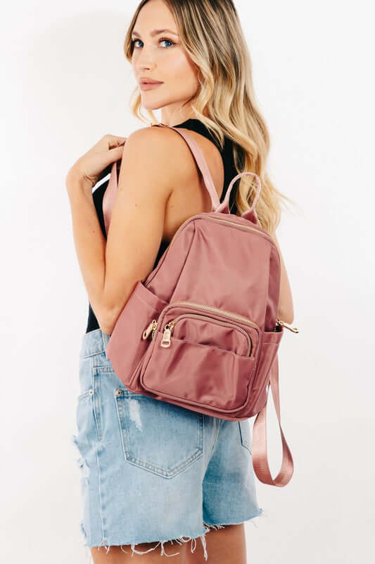 Stylish woman with medium pink nylon backpack featuring multiple pockets, perfect for daily adventures and travel.