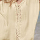 Woman wearing a cutout V-neck three-quarter sleeve cover up at the beach. Elegant sheer cover up in beige with intricate openwork detailing.