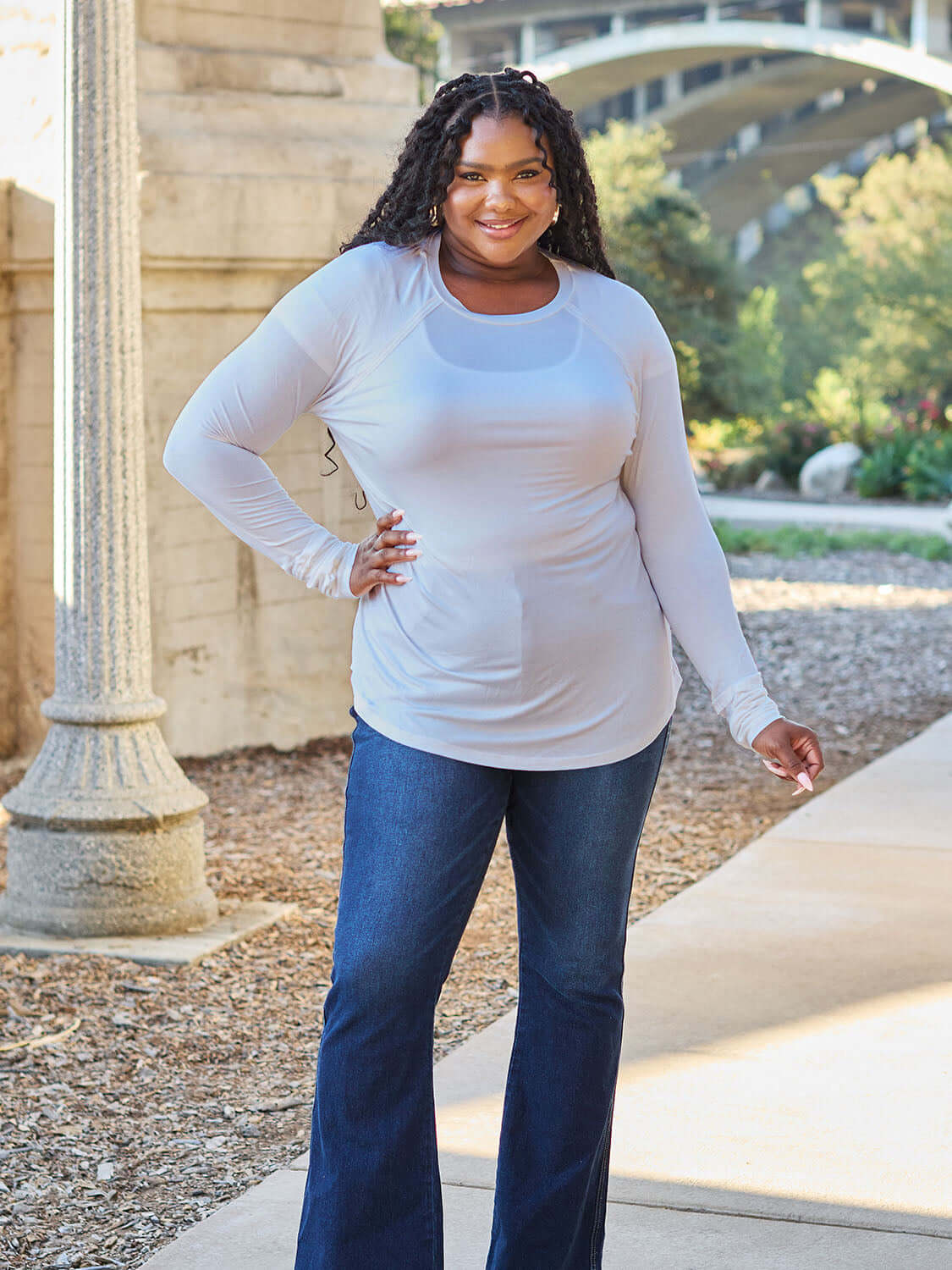 Plus-size model wearing a round neck long sleeve t-shirt with jeans, posing outdoors in a park setting