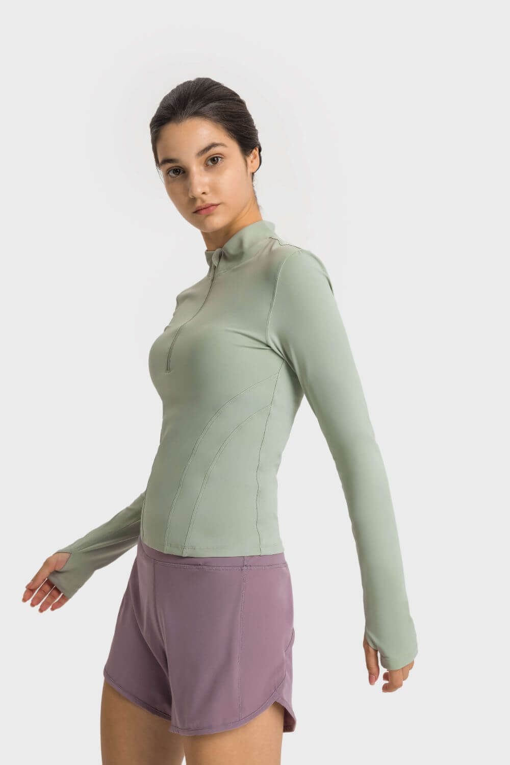 Model wearing Millennia Half Zip Thumbhole Sleeve Sports Top in green, paired with purple shorts, perfect for yoga workouts.