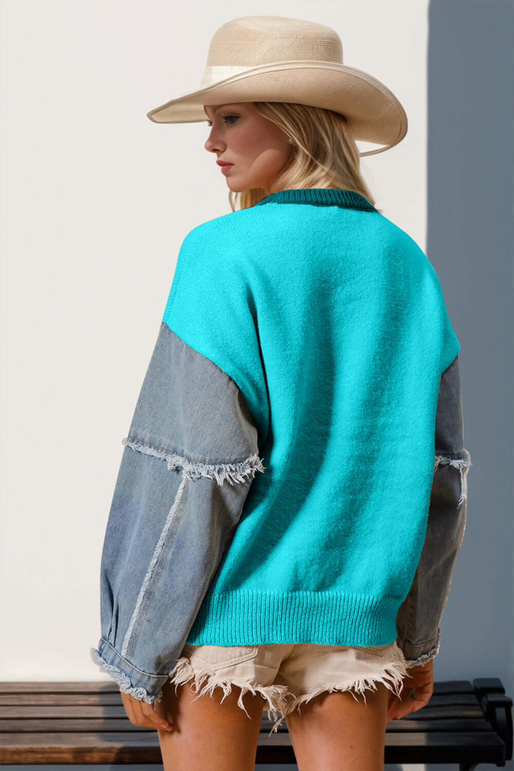 Woman wearing a turquoise long sleeve sweater with raw edges and star pattern, paired with a stylish hat and denim shorts.