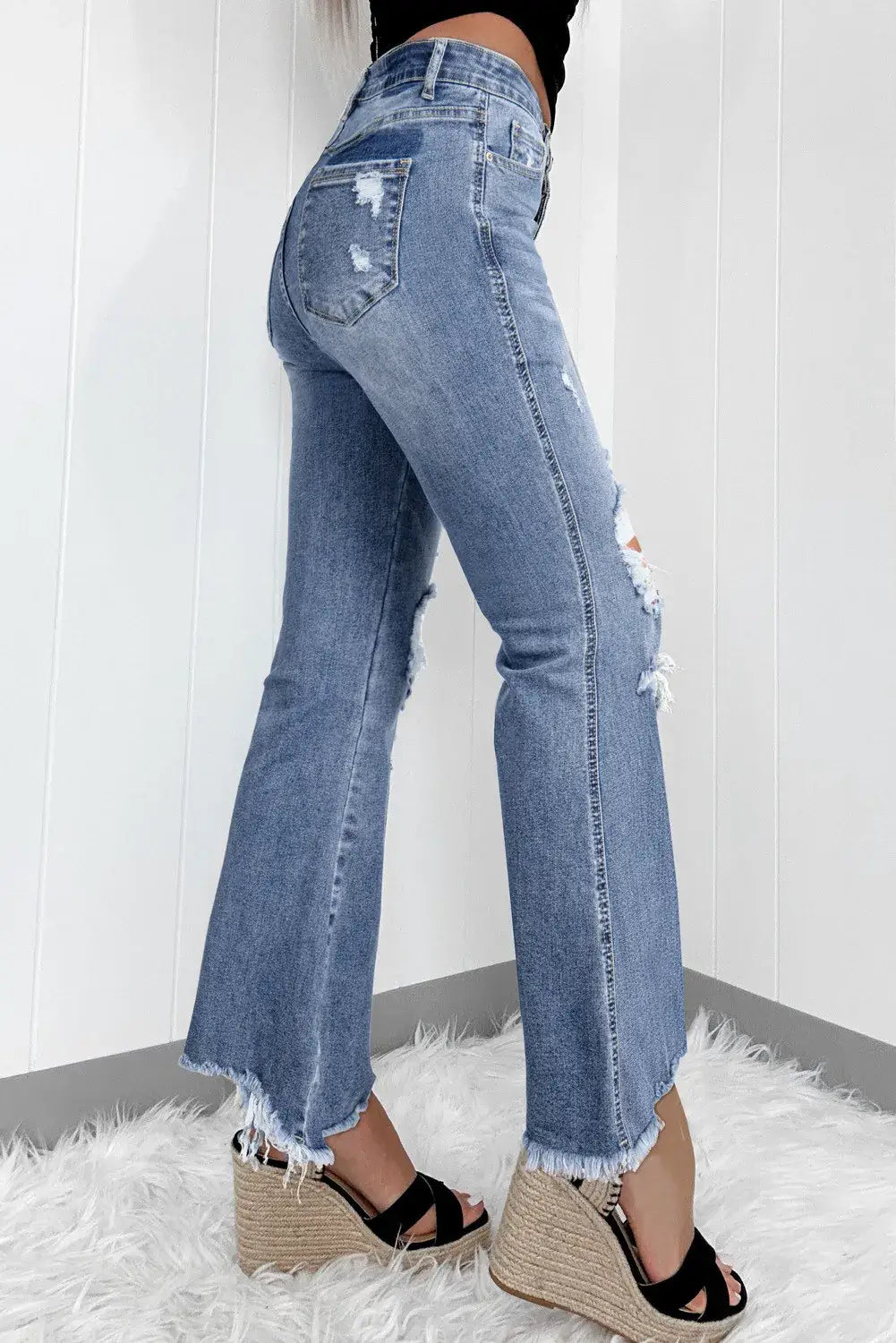 Distressed raw hem bootcut jeans with slightly stretchy material, featuring frayed edges. Styled with wedge sandals.